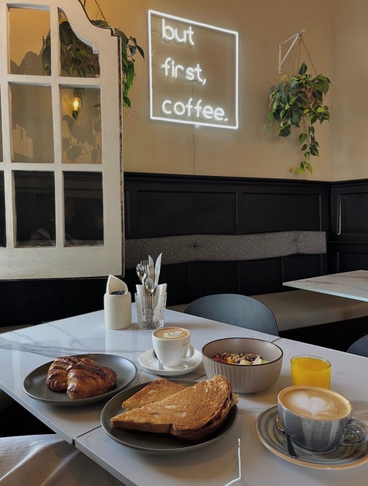 Amado Cafeteria em Montevideo - mesa com café da manhã ao estilo Uruguaio e ao fundo um quadro com a frase "But first coffee"